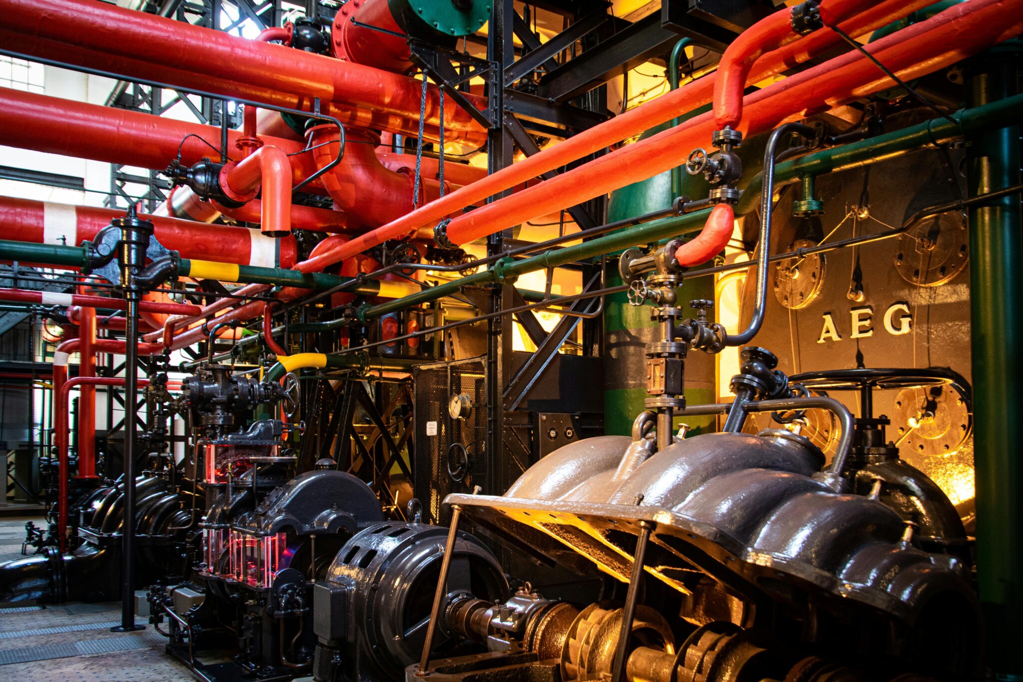 An ornate vintage power plant interior with brass valves, red pipes, and AEG generators — institutional machinery that only a few people still know how to run